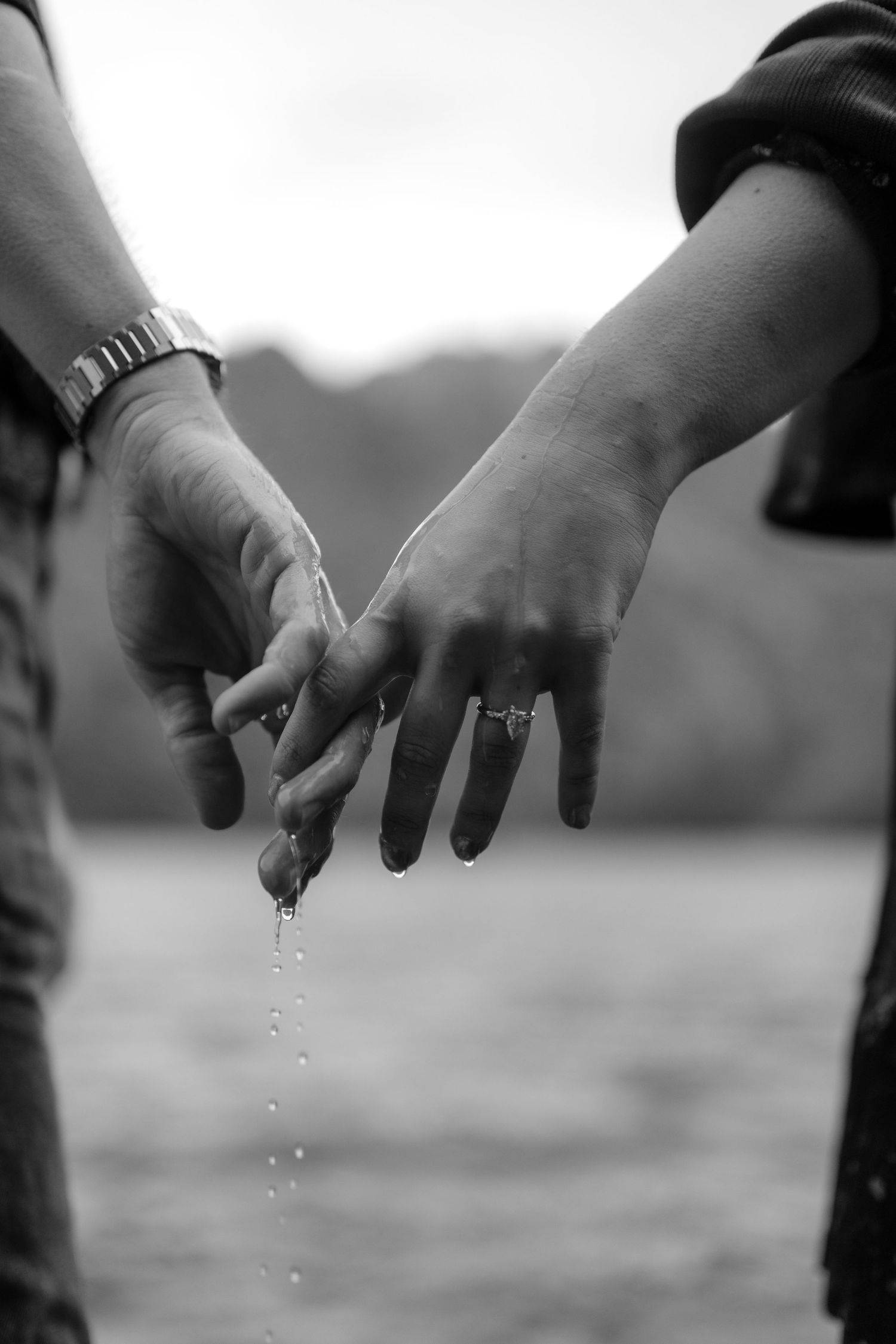 A black and white image of a couple's hands clasped together with water droplets visible.