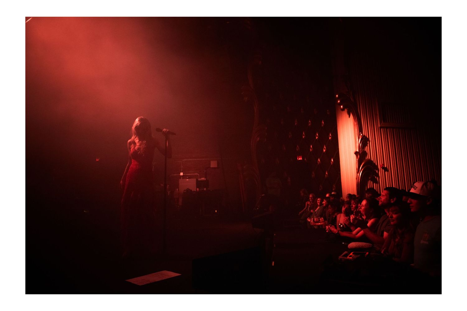 Live concert performance with a singer on stage bathed in dramatic red lighting before an audience.