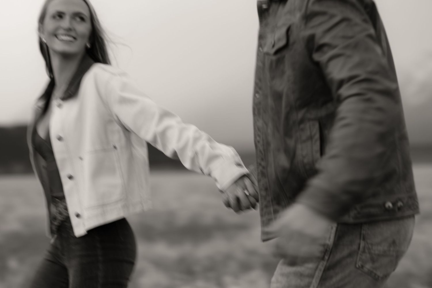Black and white photo of a couple holding hands and walking together outdoors in a field.