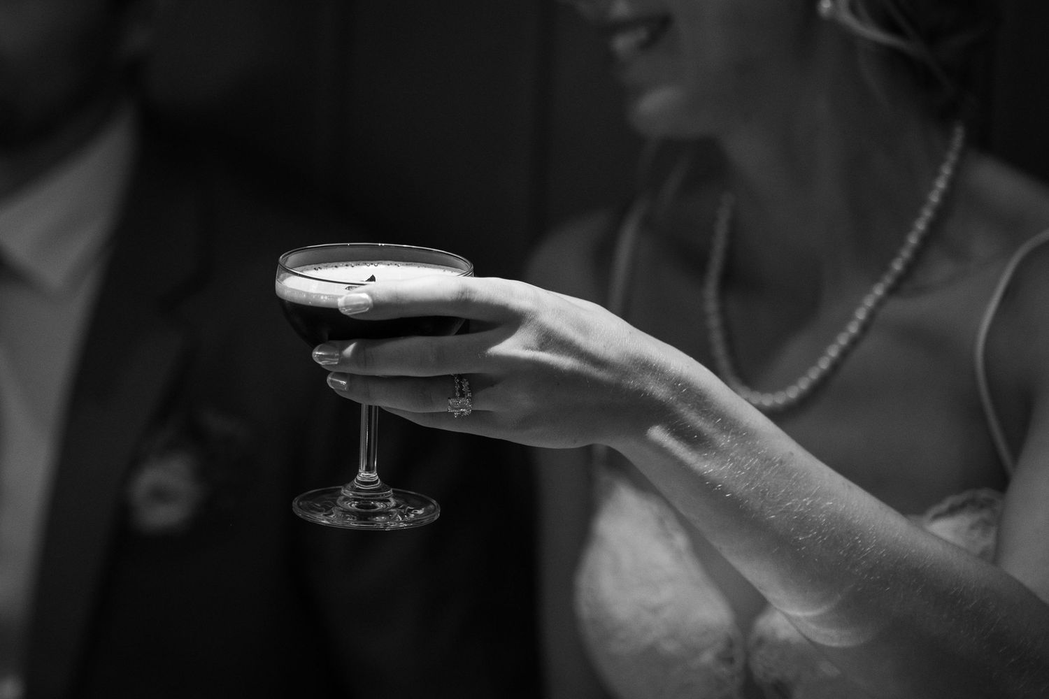Black and white photo of a bride holding a coupe glass of wine at a wedding reception.
