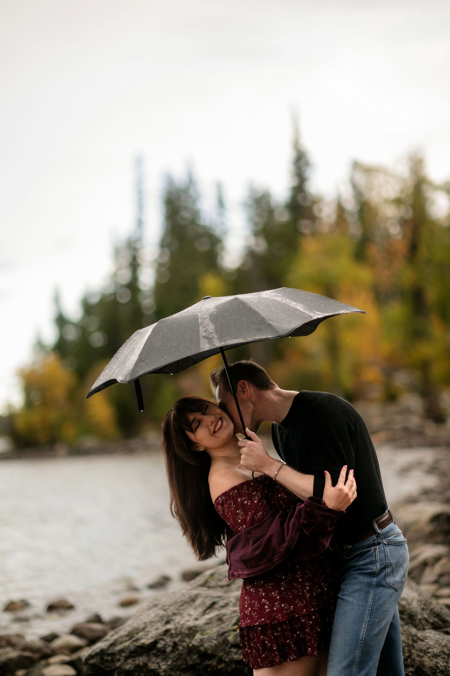 A couple embracing under an umbrella in a scenic outdoor setting.