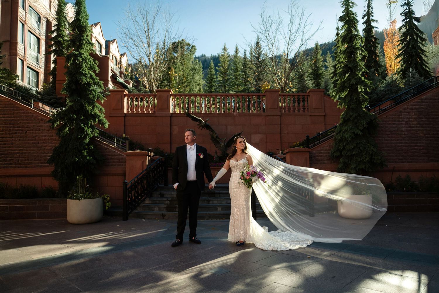 A wedding portrait captures a bride and groom standing on a stone staircase with a wooded background.