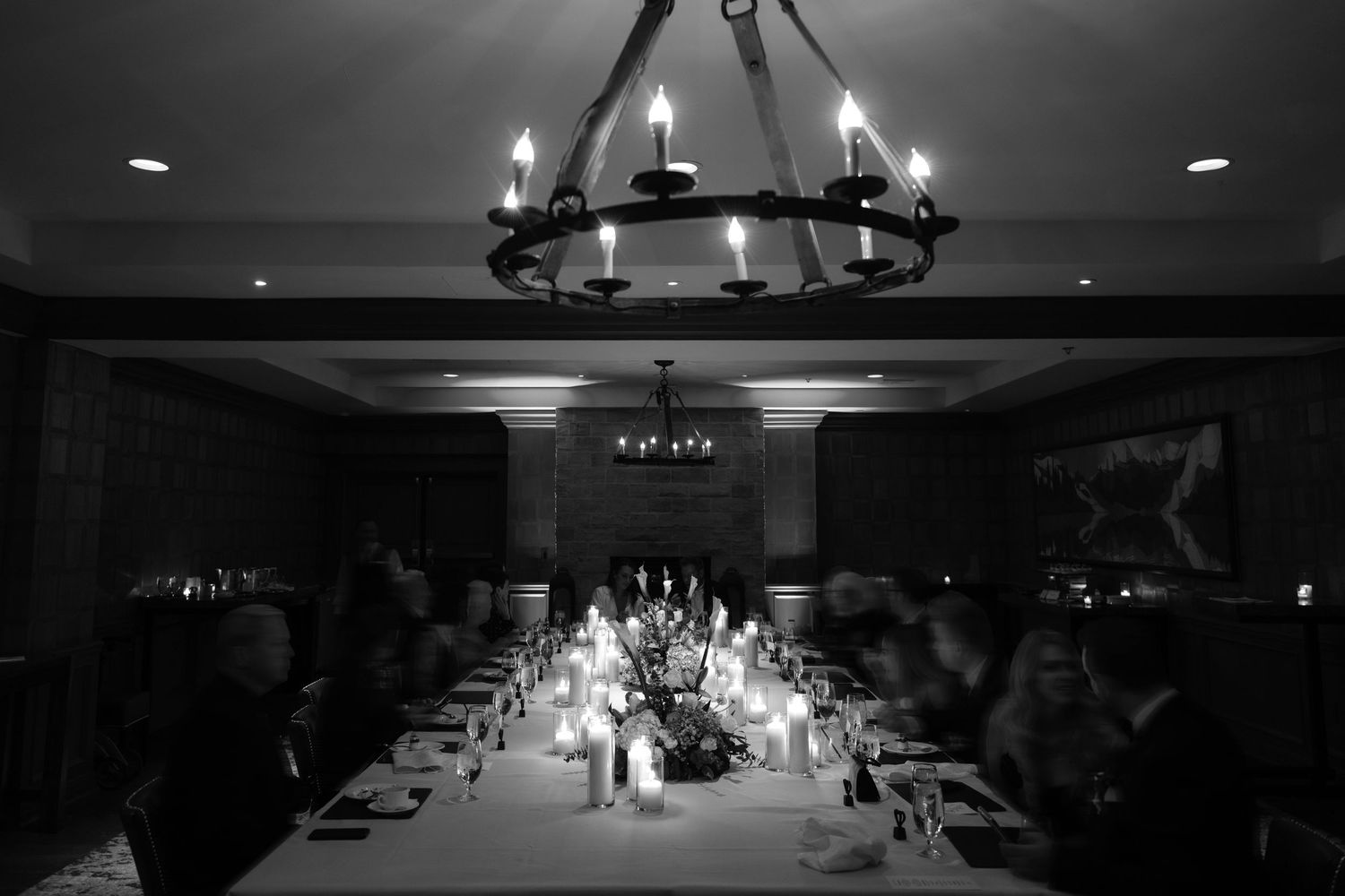 Elegant candlelit dinner party in black and white with chandelier lighting above a long formal dining table.