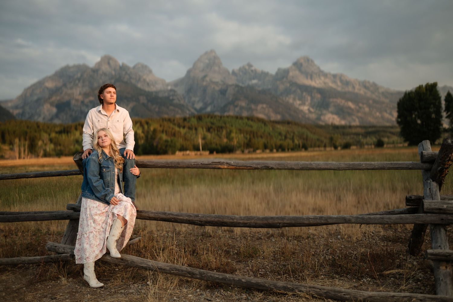 A man and woman standing in a field with mountains in the distance.