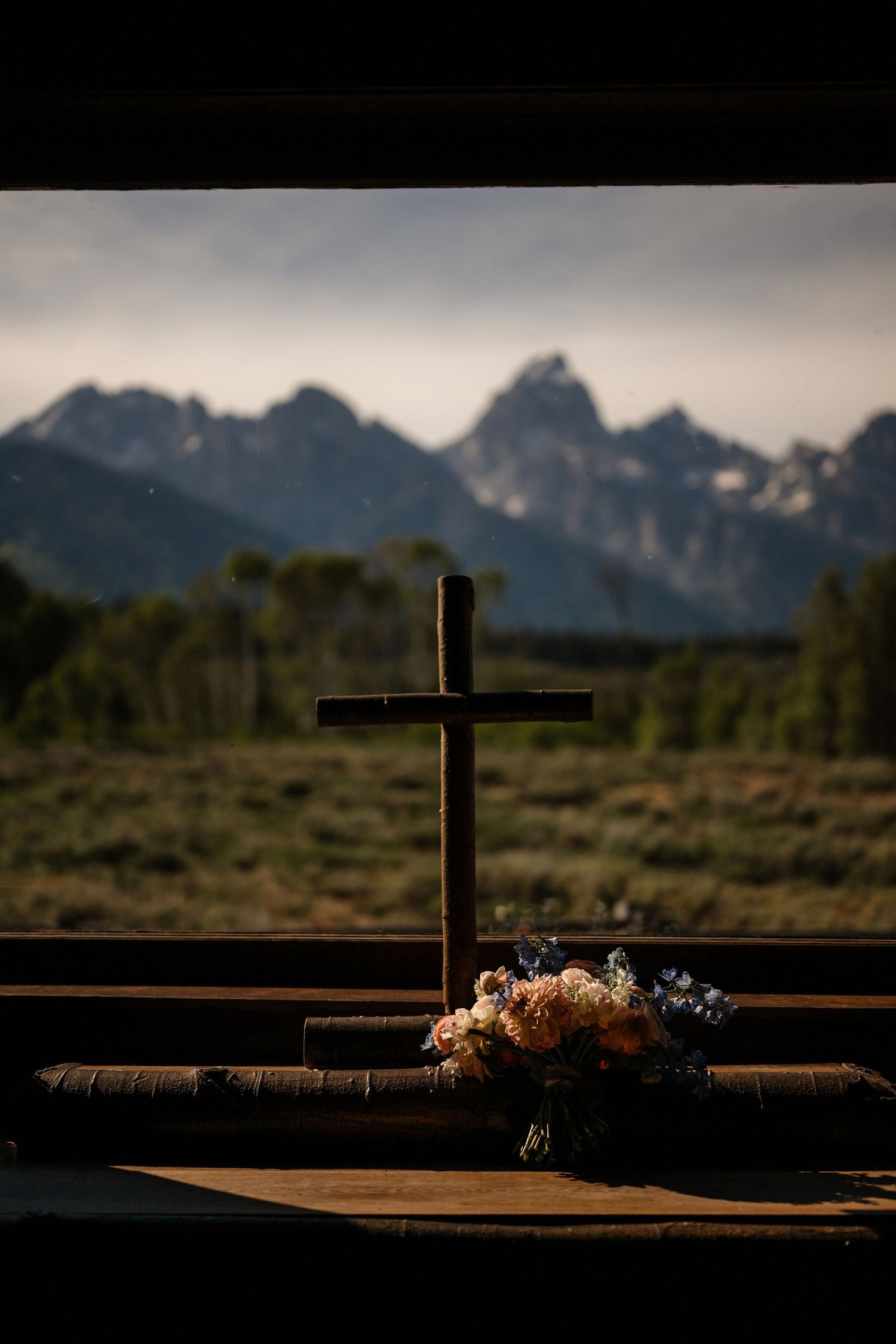 Wooden cross with floral bouquet inside a rustic chapel overlooking the Grand Teton mountains in Wyoming.