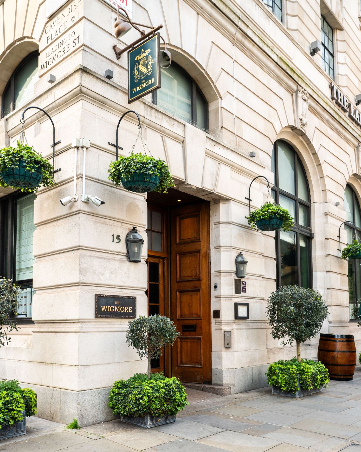 Elegant entrance of The Wigmore pub at 15 Wigmore Street, London, featuring stone facade, hanging plants, and wooden doors.