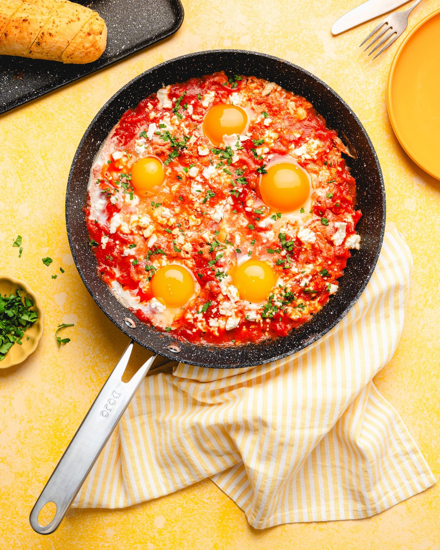 Shakshuka with poached eggs in tomato sauce, topped with feta and herbs, served in a skillet on a yellow background.