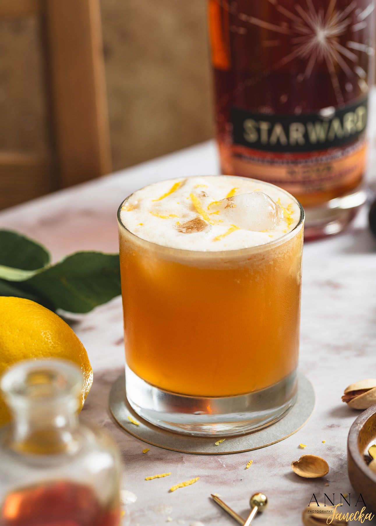 Orange-colored cocktail garnished with foam in a glass tumbler.