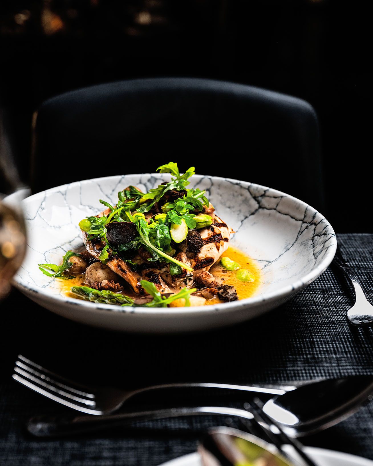 Elegant restaurant dish featuring grilled fish topped with fresh arugula, asparagus, and carrots in a decorative ceramic bowl.