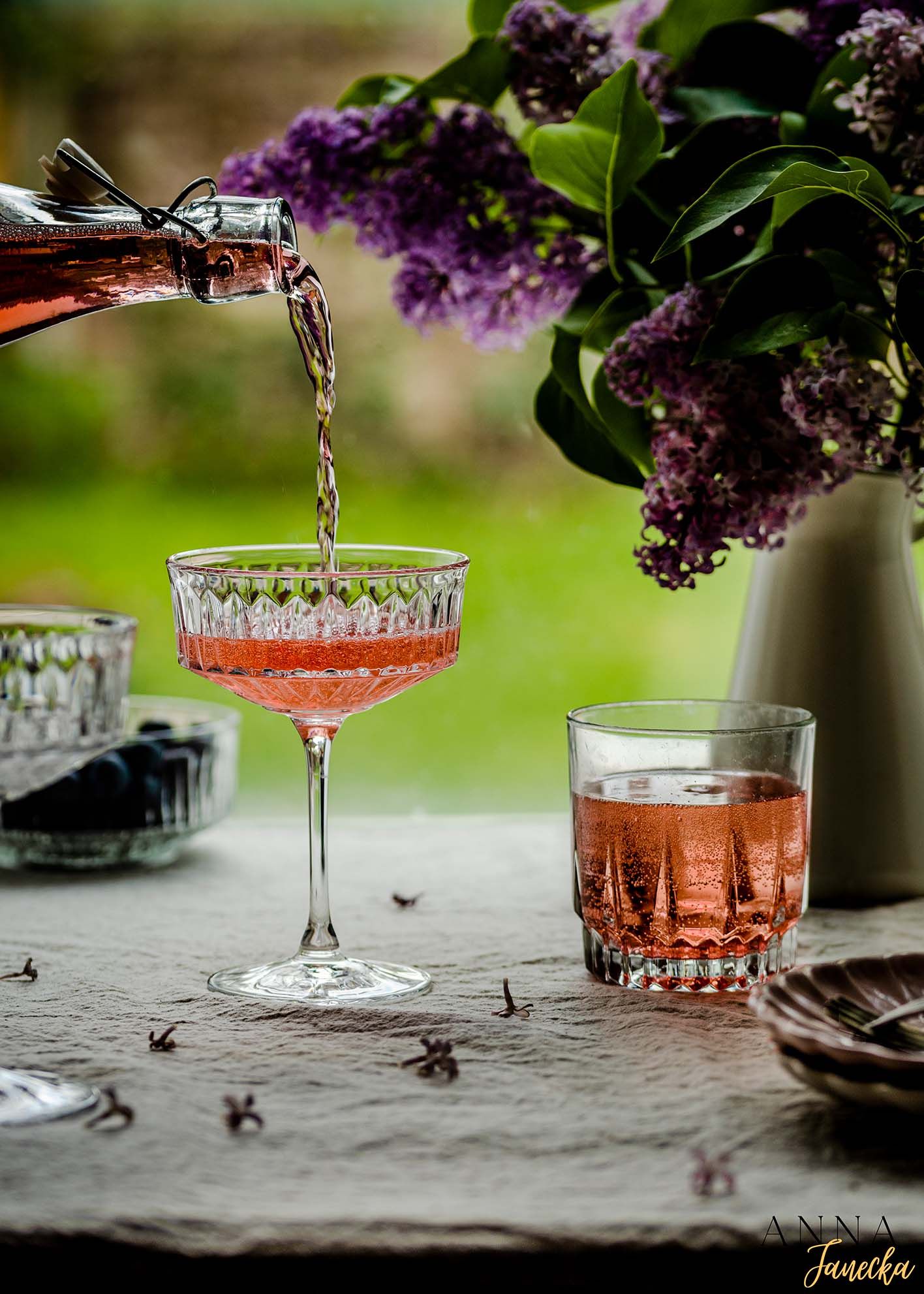Pink cocktails in vintage coupe glasses with lilac flowers in the background.