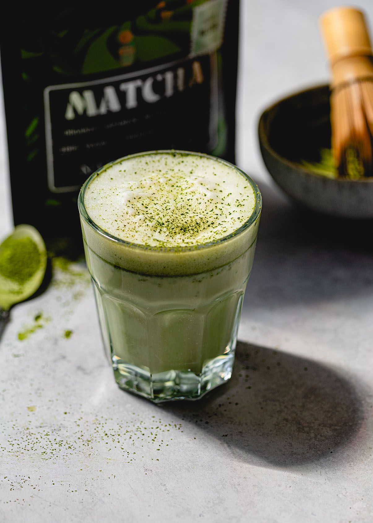 Matcha green tea latte topped with powder in a clear glass with lime garnish.