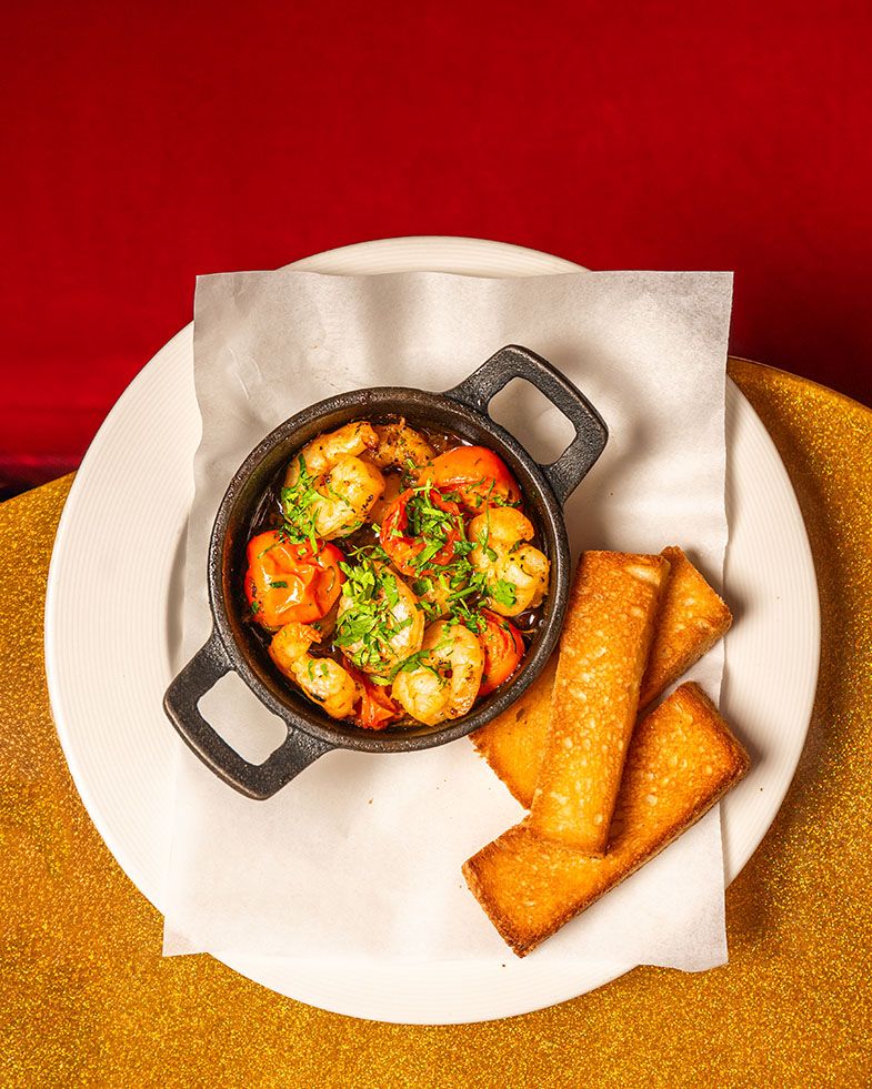 Cast iron pan of saucy shrimp with herbs served with golden toasted bread slices on white plate.