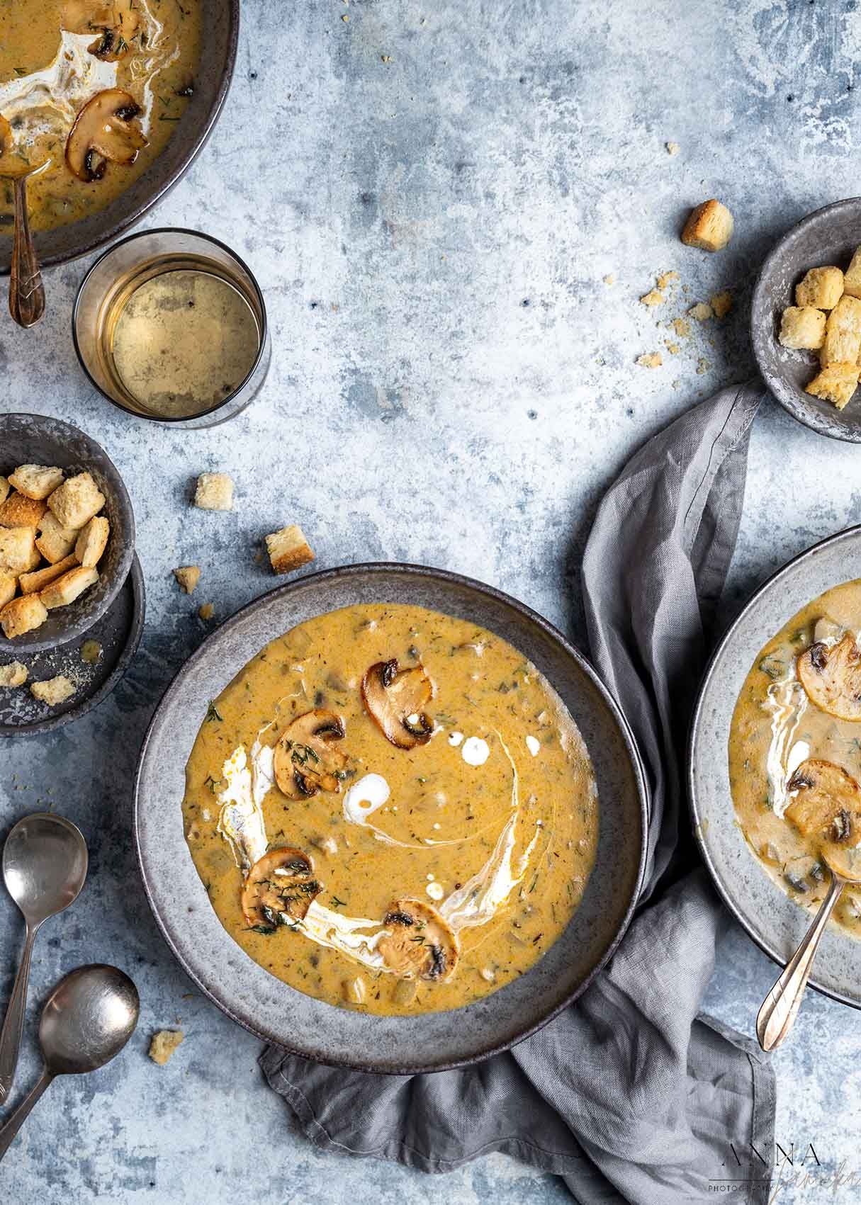 Creamy mushroom soup with croutons and swirls of cream served in gray bowls.