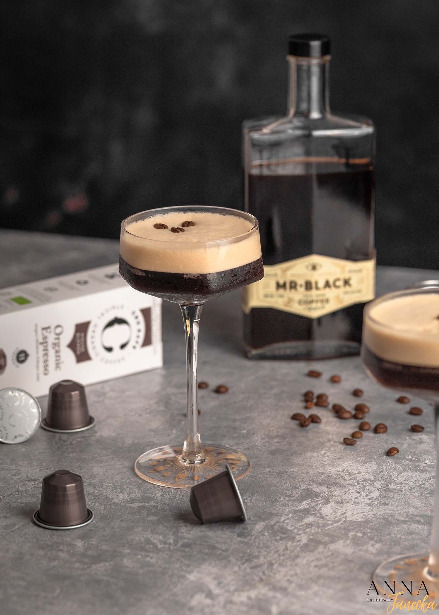 Espresso martini cocktail with creamy foam and coffee beans on dark background.