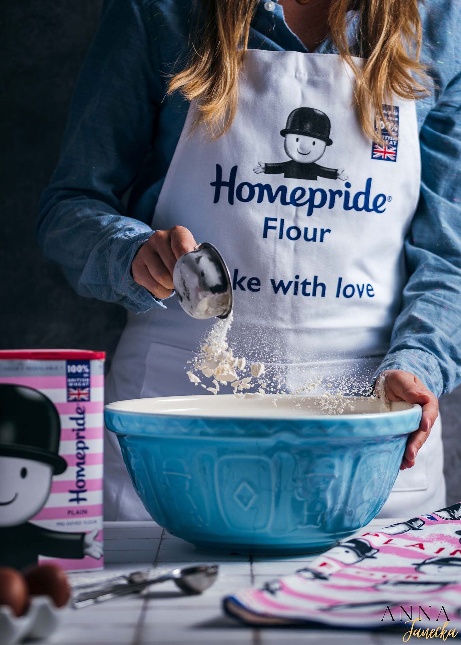 Hands mixing ingredients in blue ceramic bowls with flour and baking supplies.