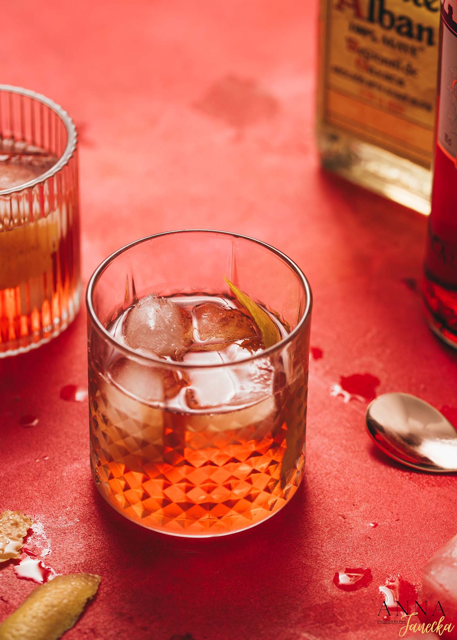 Whiskey cocktail with ice in a textured glass on red background.