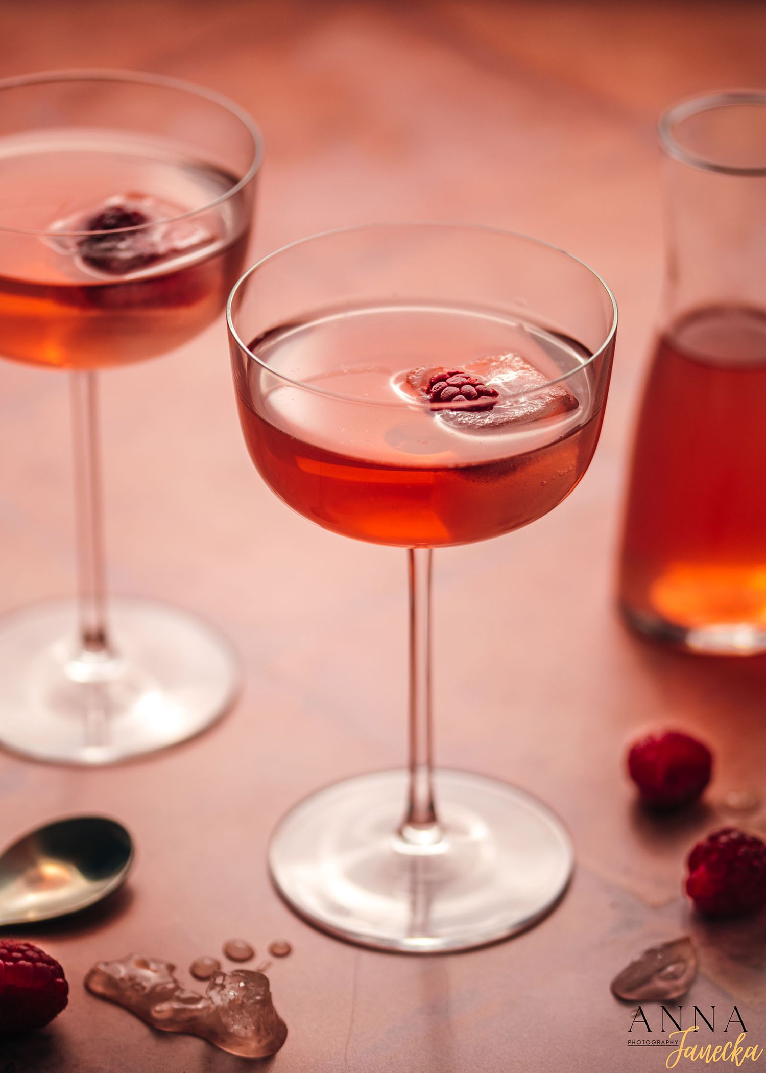 Pink cocktails with raspberries served in elegant coupe glasses on a rosy background.