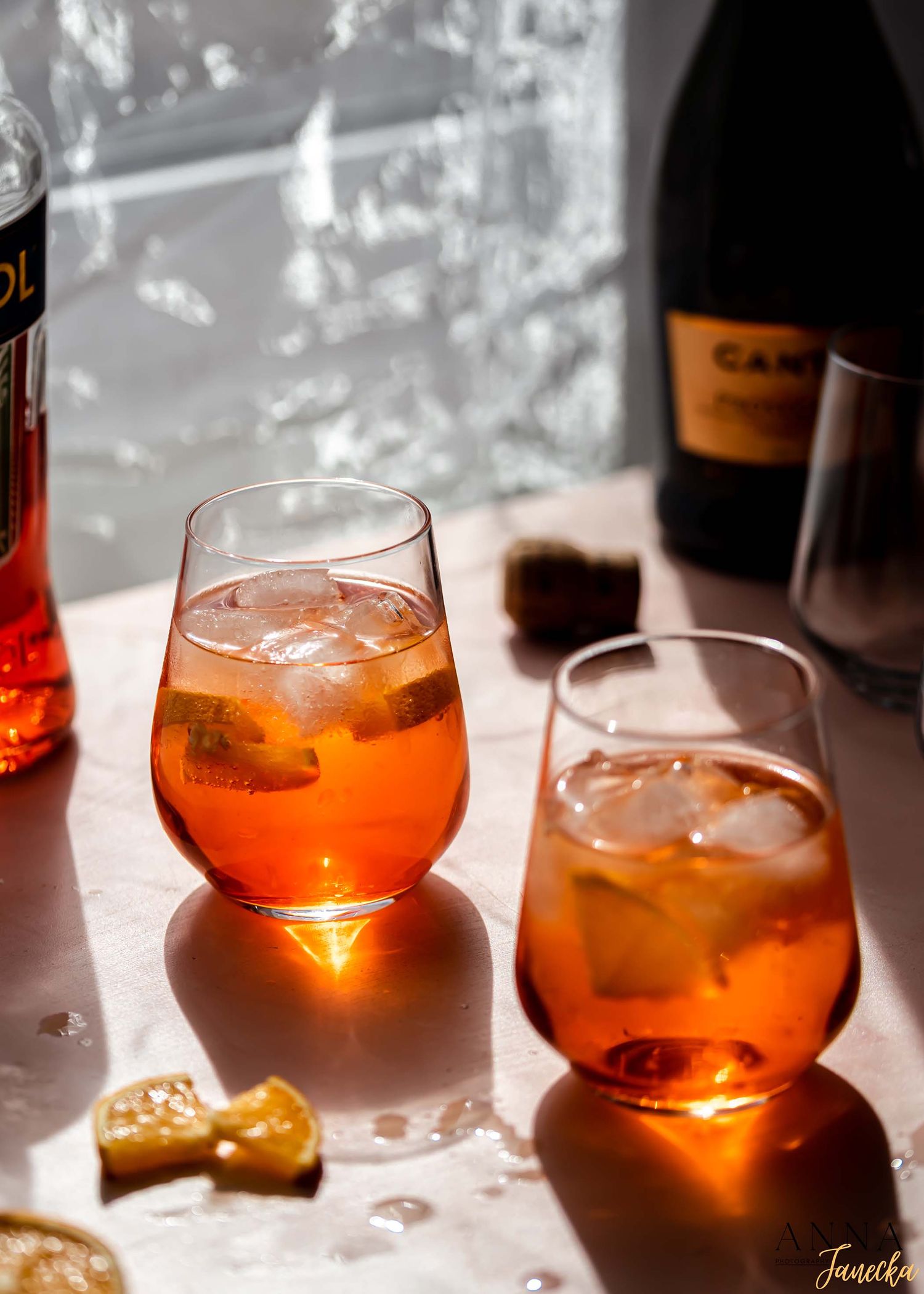 Orange-hued cocktails with ice in rocks glasses lined up on a counter.