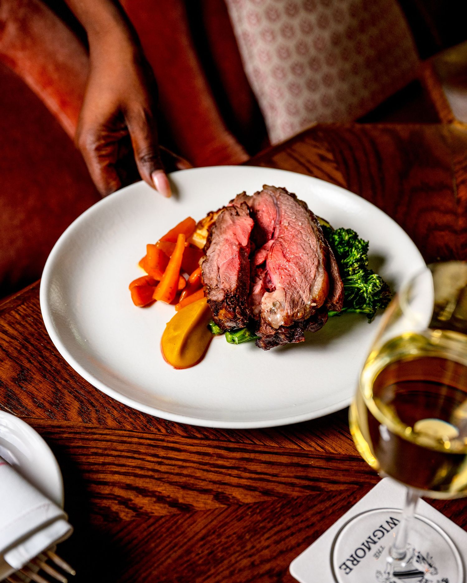 Elegant plated medium-rare roast beef with carrots, broccoli, and white wine at a fine dining restaurant.
