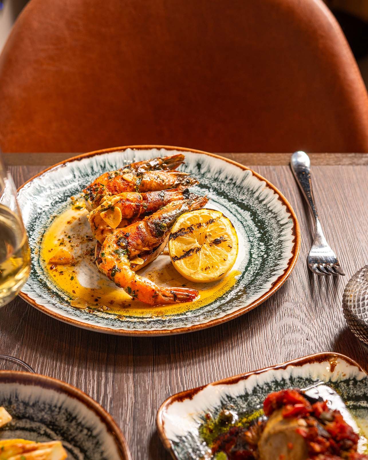 Grilled shrimp with lemon slices in creamy sauce served on a decorative ceramic plate at a restaurant.
