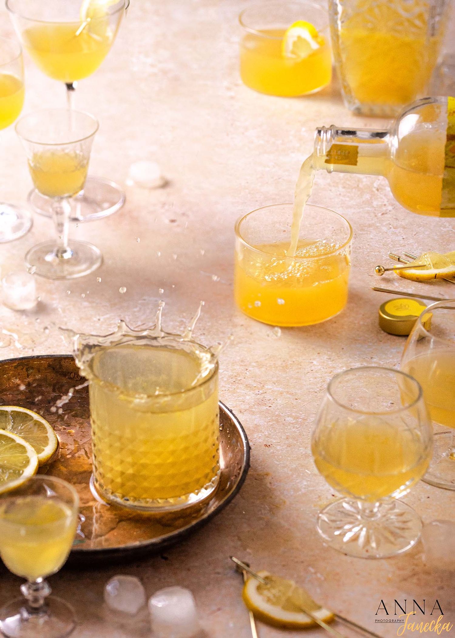 Various glasses filled with bright yellow citrus cocktails garnished with lemon slices on a rustic surface.