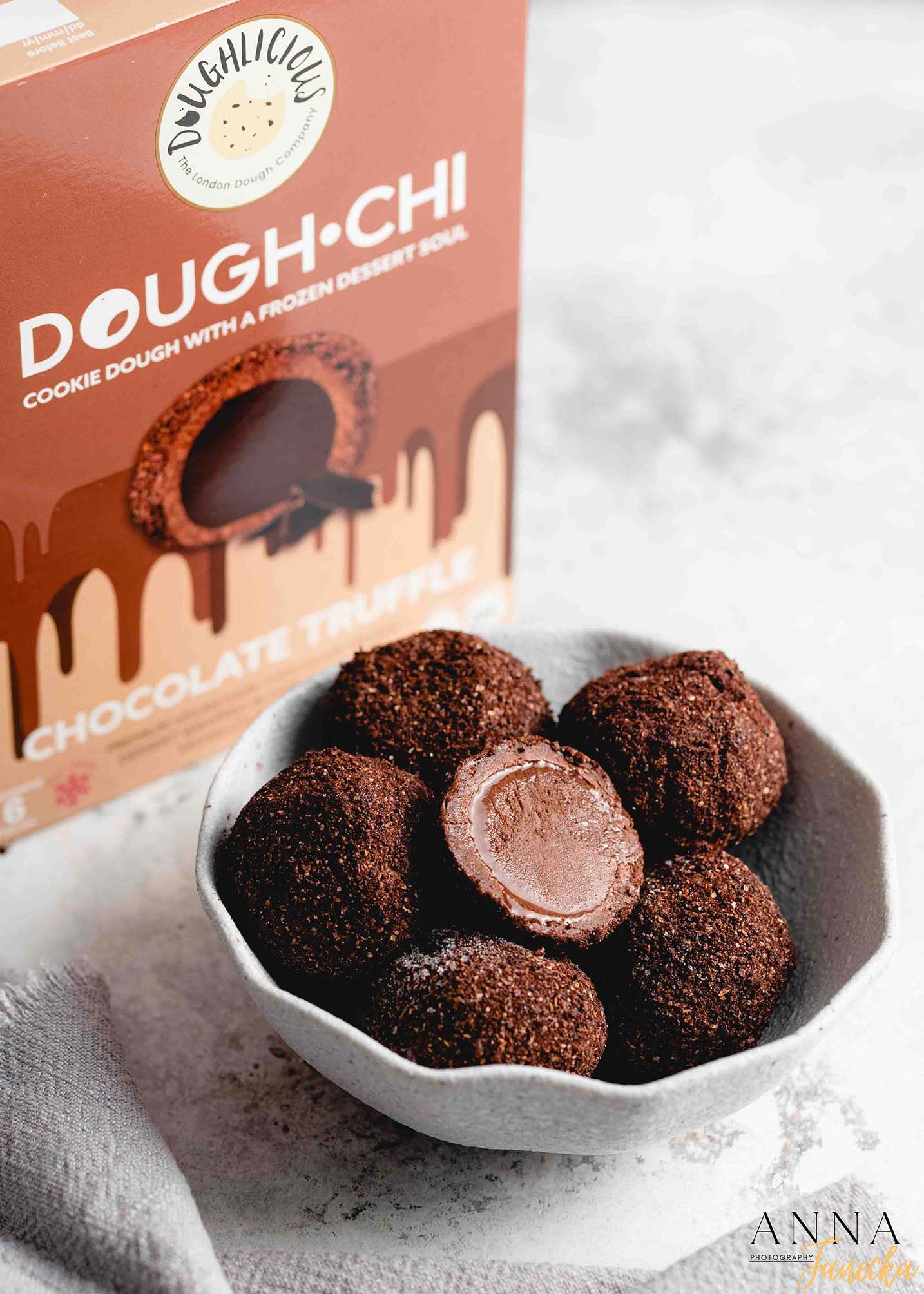 Bowl of chocolate coated Dough-Chi cookie dough balls with product packaging.