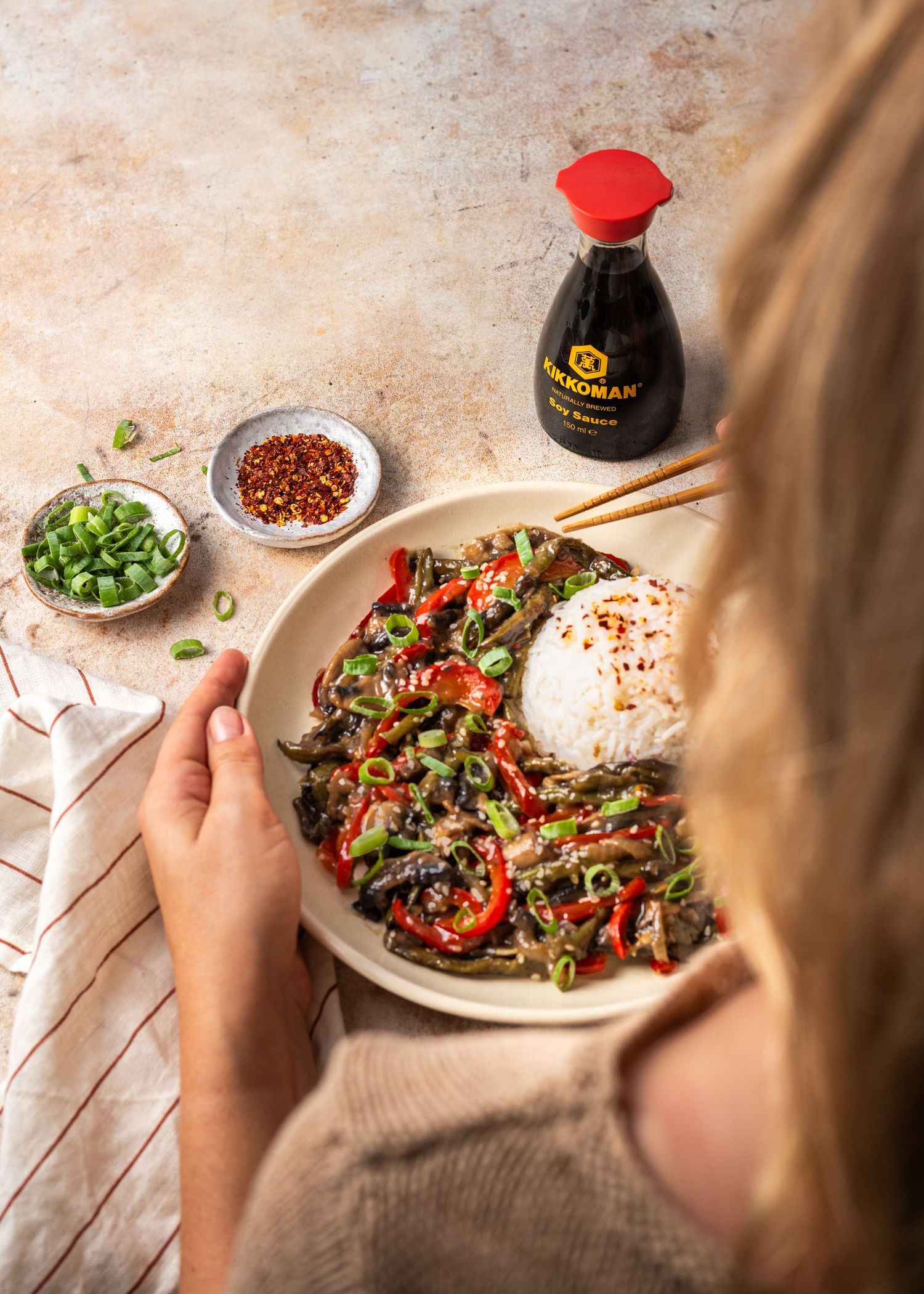 Asian stir fry dish with rice being garnished with green onions on white plate.