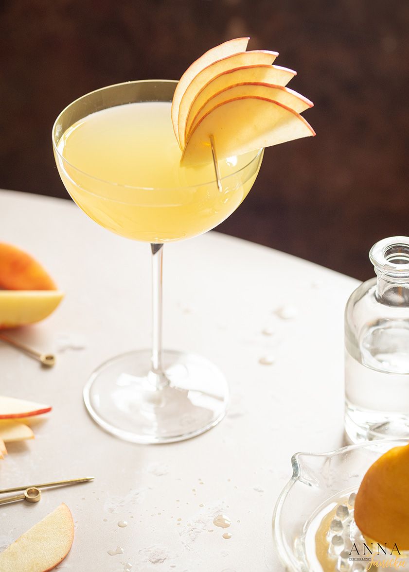 Yellow citrus cocktail garnished with fresh apple slices in a martini glass.
