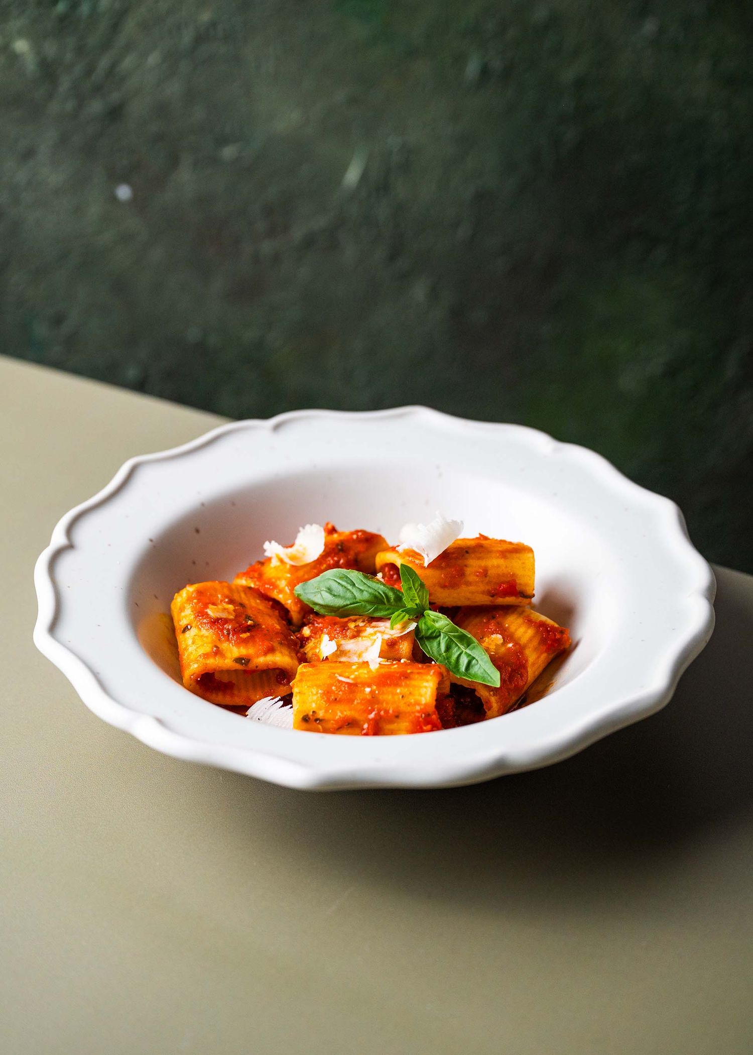 Ravioli pasta with tomato sauce and fresh basil garnish served on a white scalloped plate.
