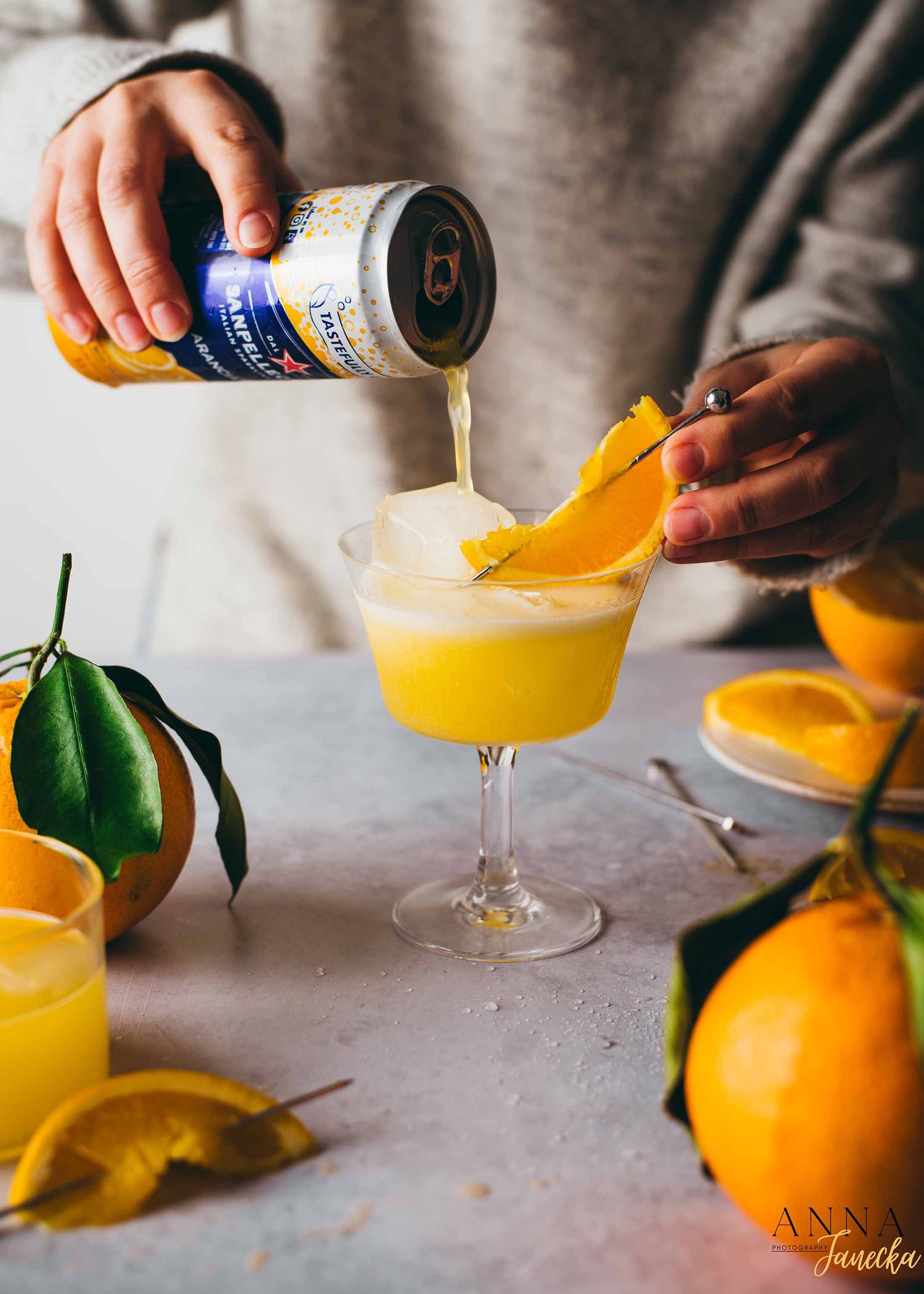 Pouring orange juice cocktails into glasses with fresh citrus garnish.
