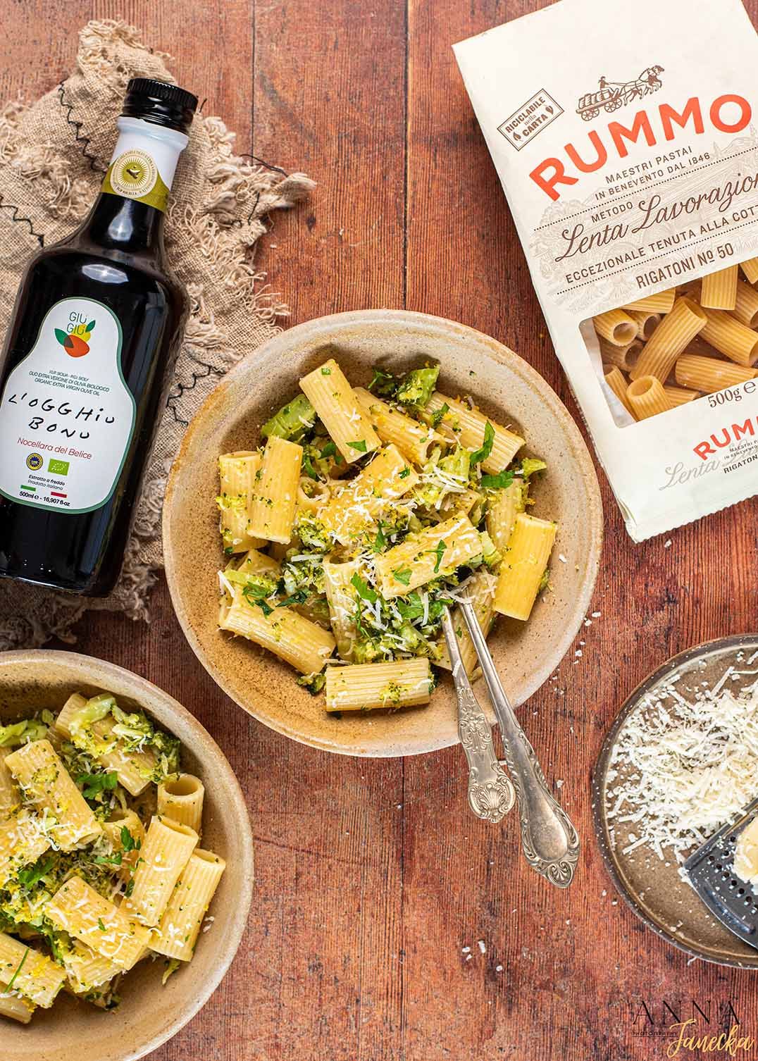 Pasta dishes served with cheese and herbs on wooden table with bottles of wine and spirits.
