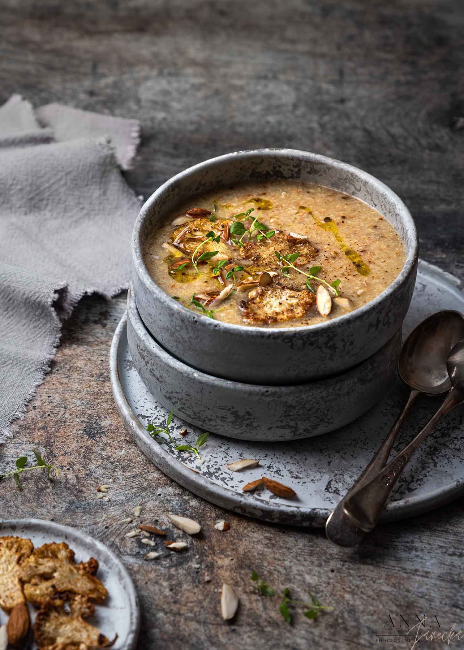 Creamy soup served in stone bowls garnished with herbs and nuts on rustic surface.