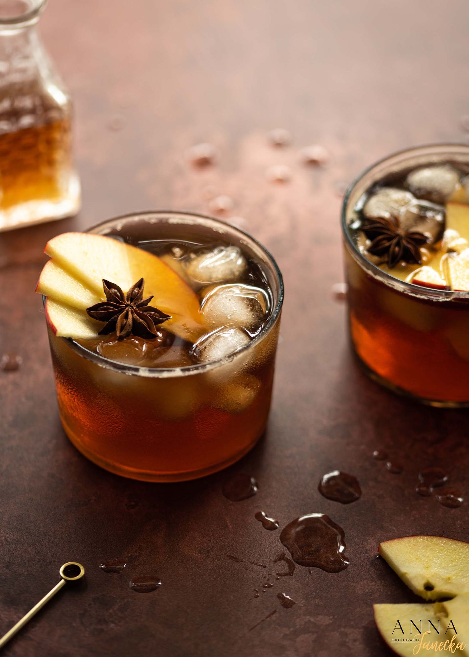 Dark cocktails garnished with star anise, orange peel and ice in rocks glasses.