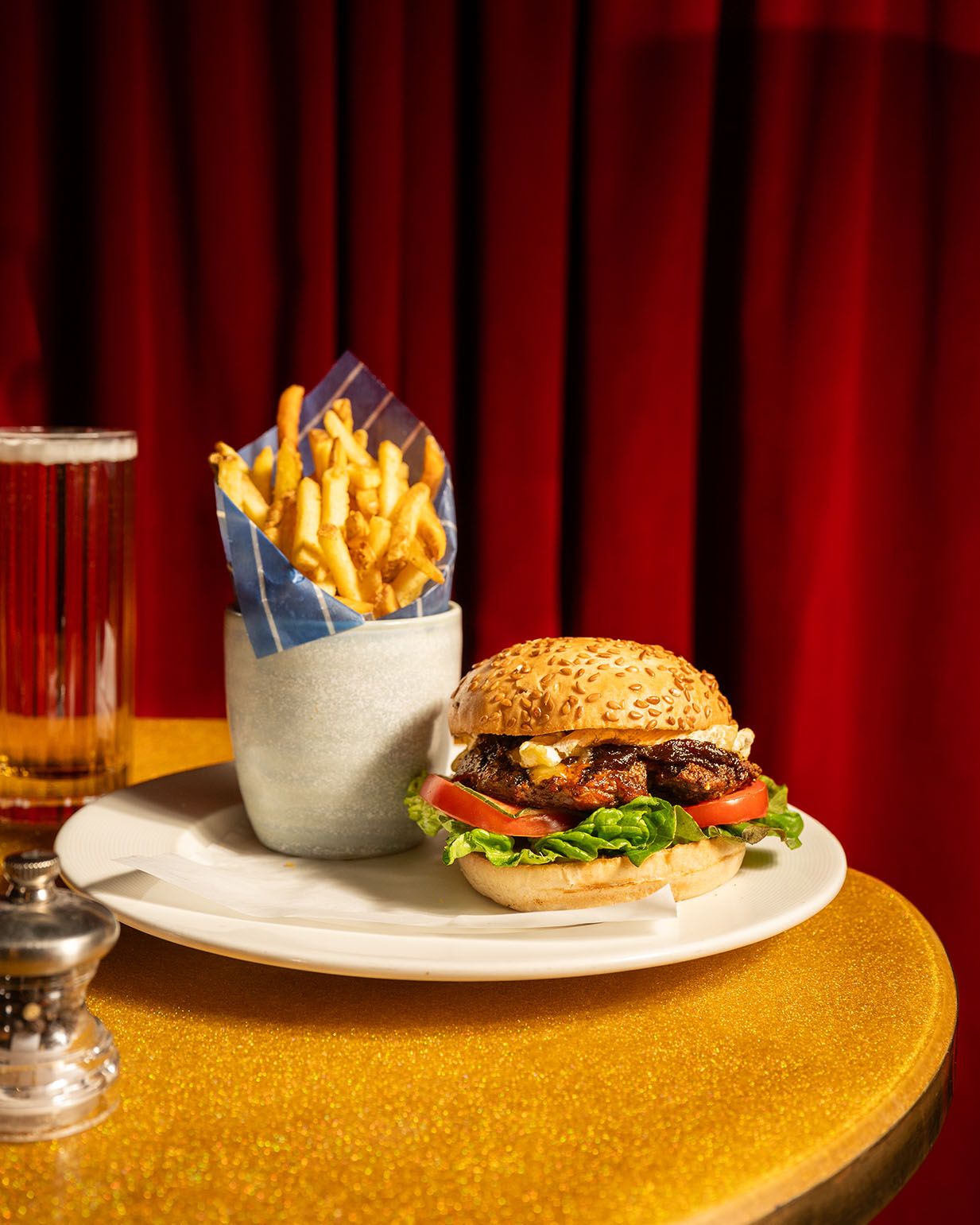 A classic burger with lettuce and tomato on a sesame bun, served with crispy fries on a white plate.