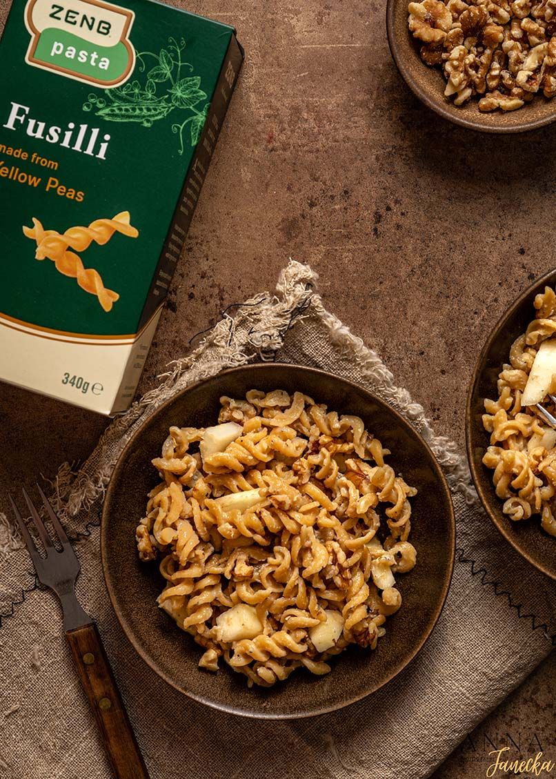 Fusilli pasta with walnuts served in a rustic dark bowl with ZENB yellow pea pasta package.
