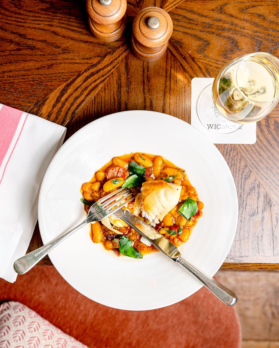 Overhead view of a gourmet chicken dish with tomato gnocchi on a white plate, served with white wine at a restaurant.