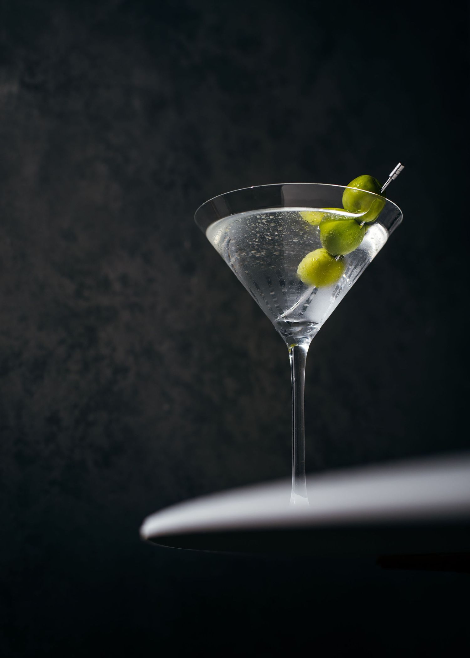Classic martini cocktail with green olives in a stemmed glass against dark background.