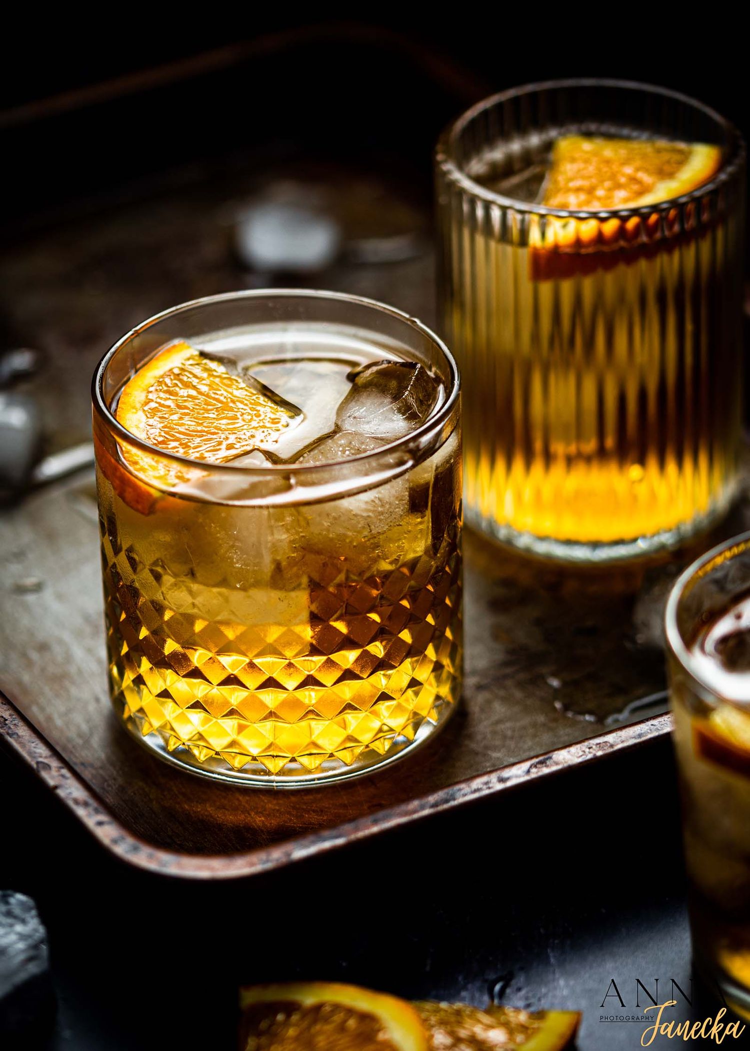 Old fashioned cocktails with orange garnish served in crystal glasses on a dark background.