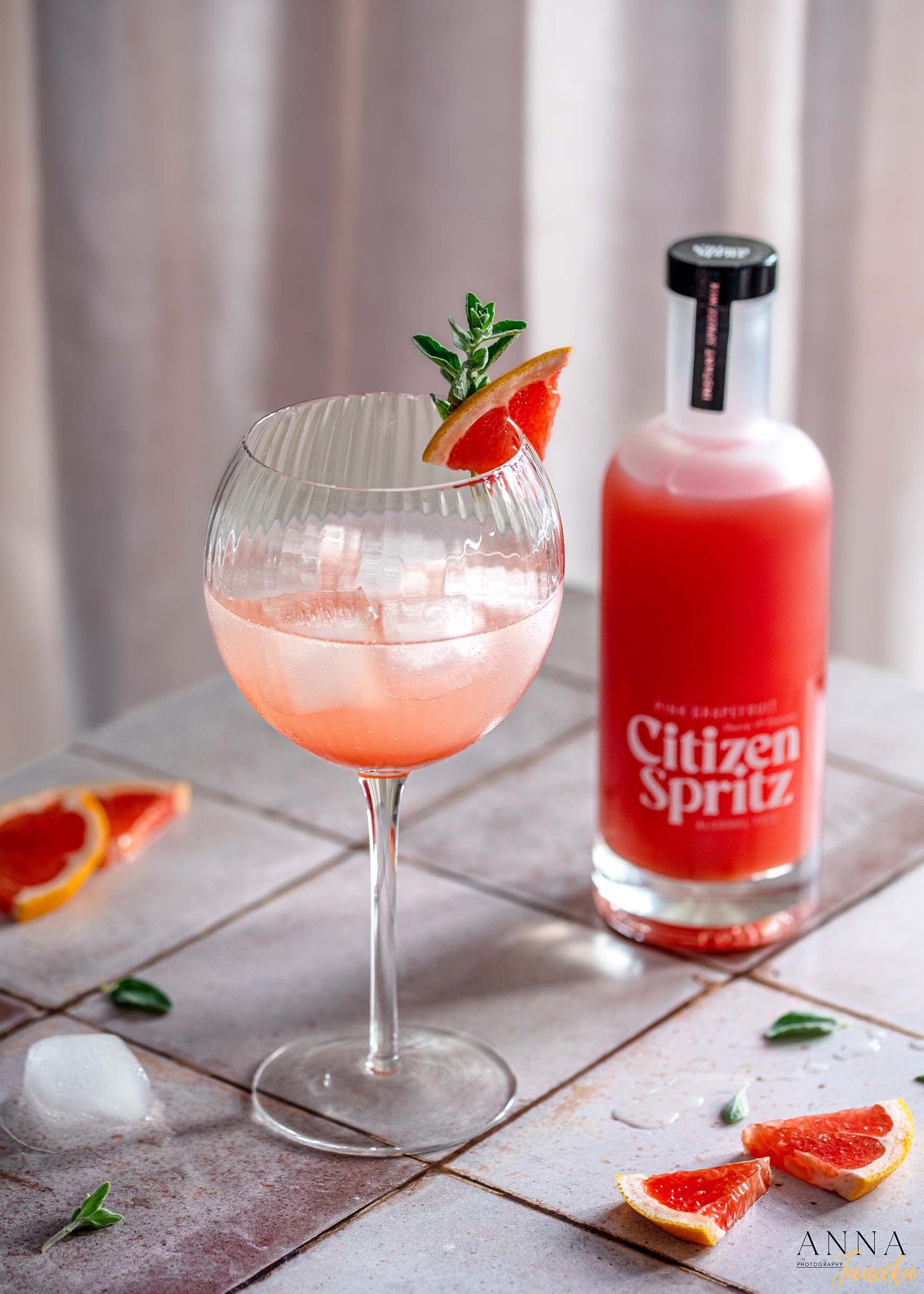 Colorful spritz cocktails garnished with citrus and herbs on white wooden surface.