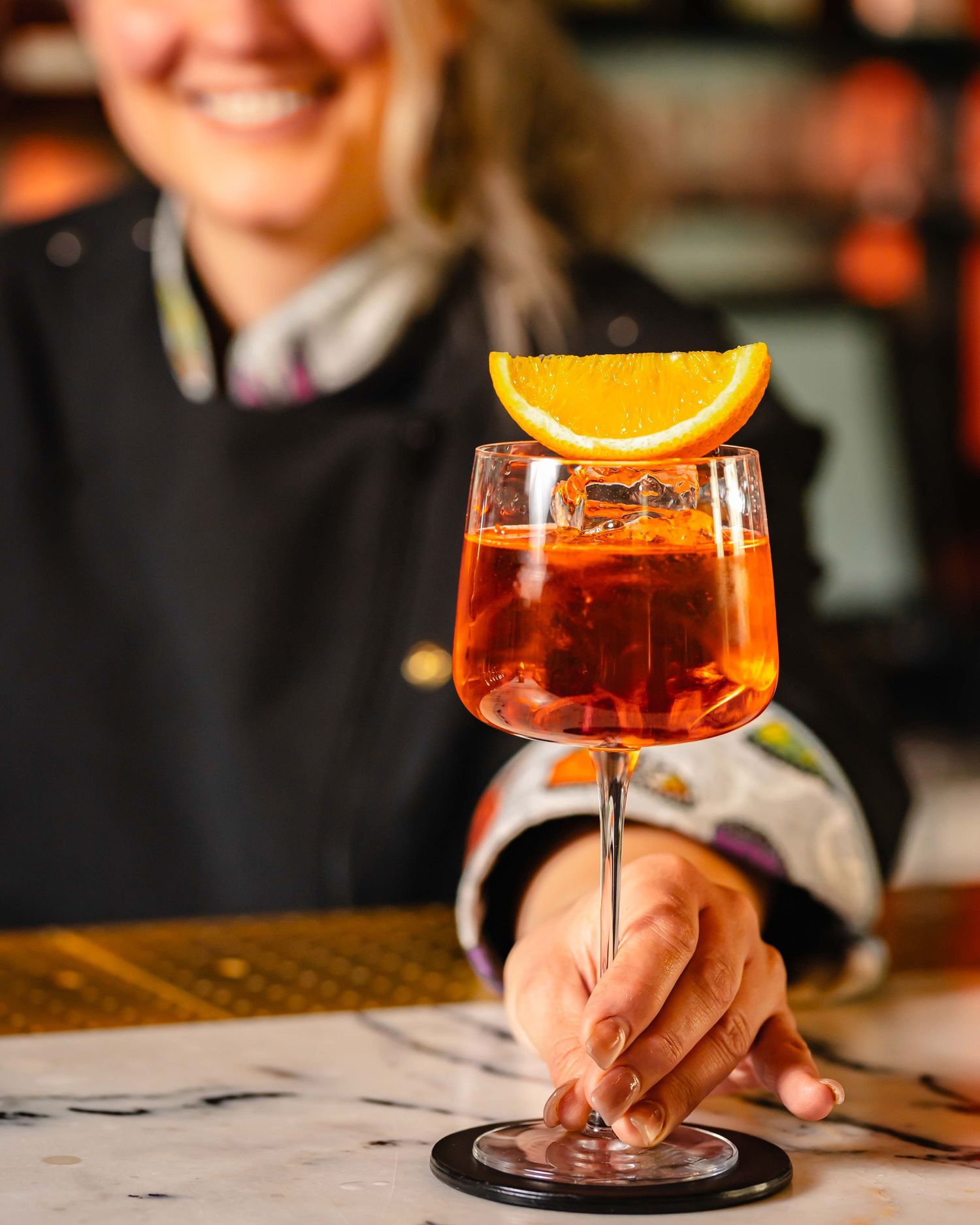 Bartender presenting a classic Aperol Spritz cocktail garnished with an orange slice in a stemmed glass.