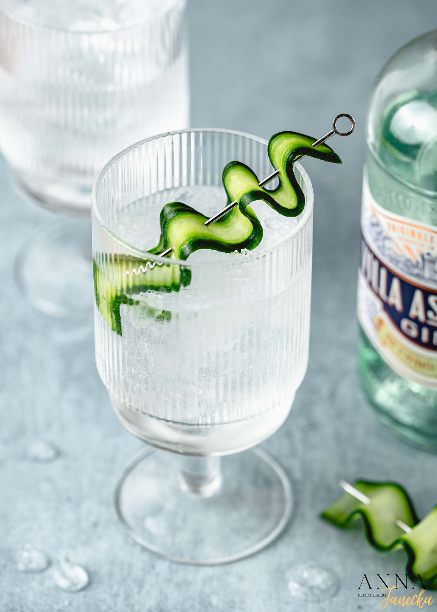 Clear cocktail glass with spiral cucumber garnish and ice cubes.