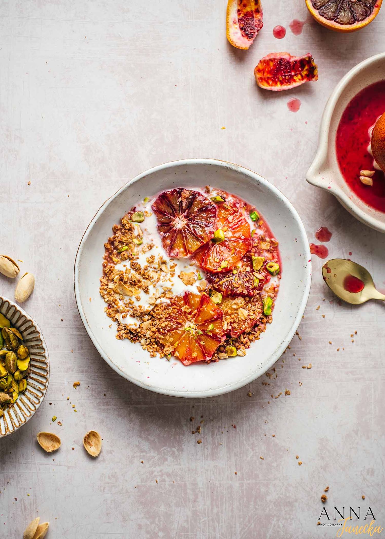 Breakfast bowl with granola, blood orange slices, and yogurt on a light surface.