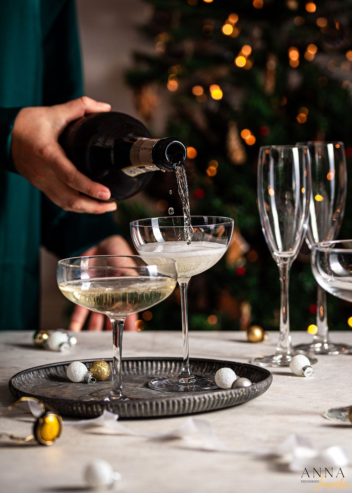 Champagne coupe glasses being arranged on a dark tray with holiday ornaments.
