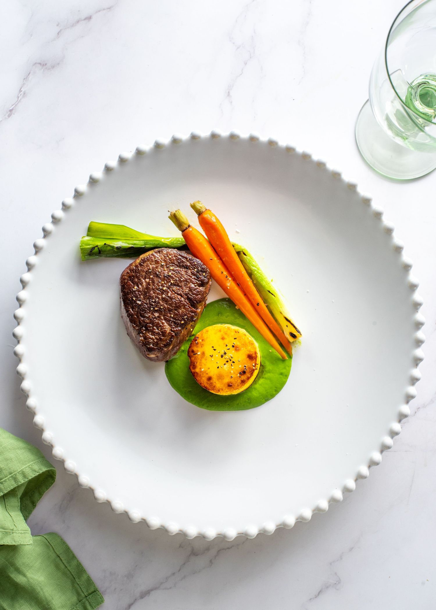 White plated dish with carrots and meatballs on marble surface.
