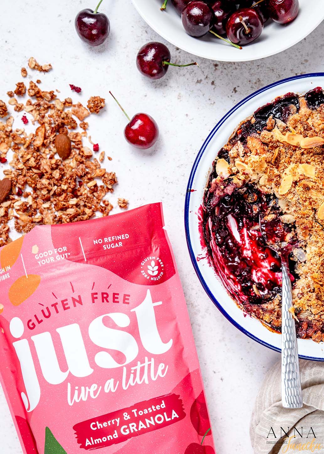 Fresh cherries and granola scattered around a fruit crumble dessert in blue and white dish.