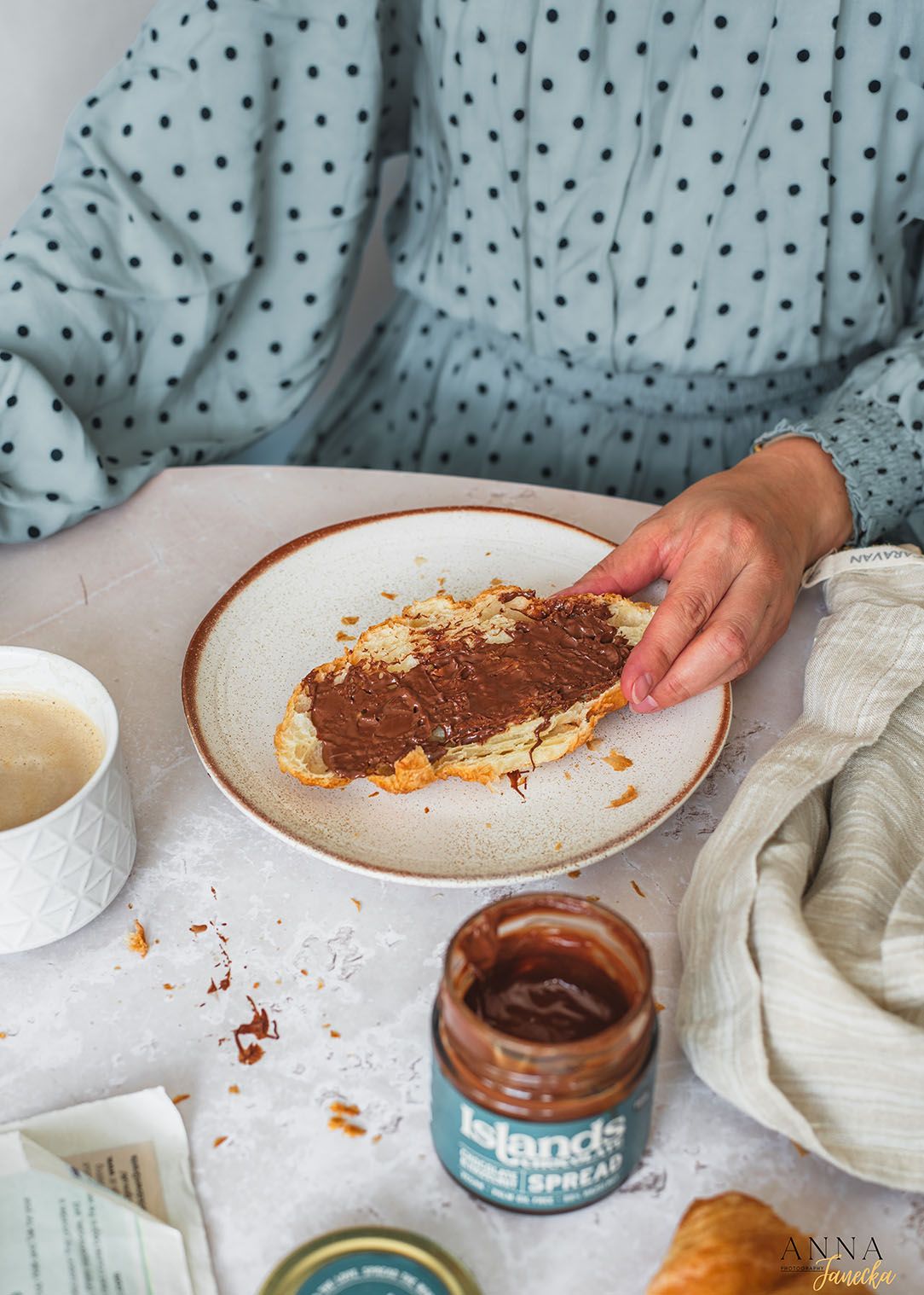 Spreading chocolate spread on toast with a jar of spread and coffee cup nearby.