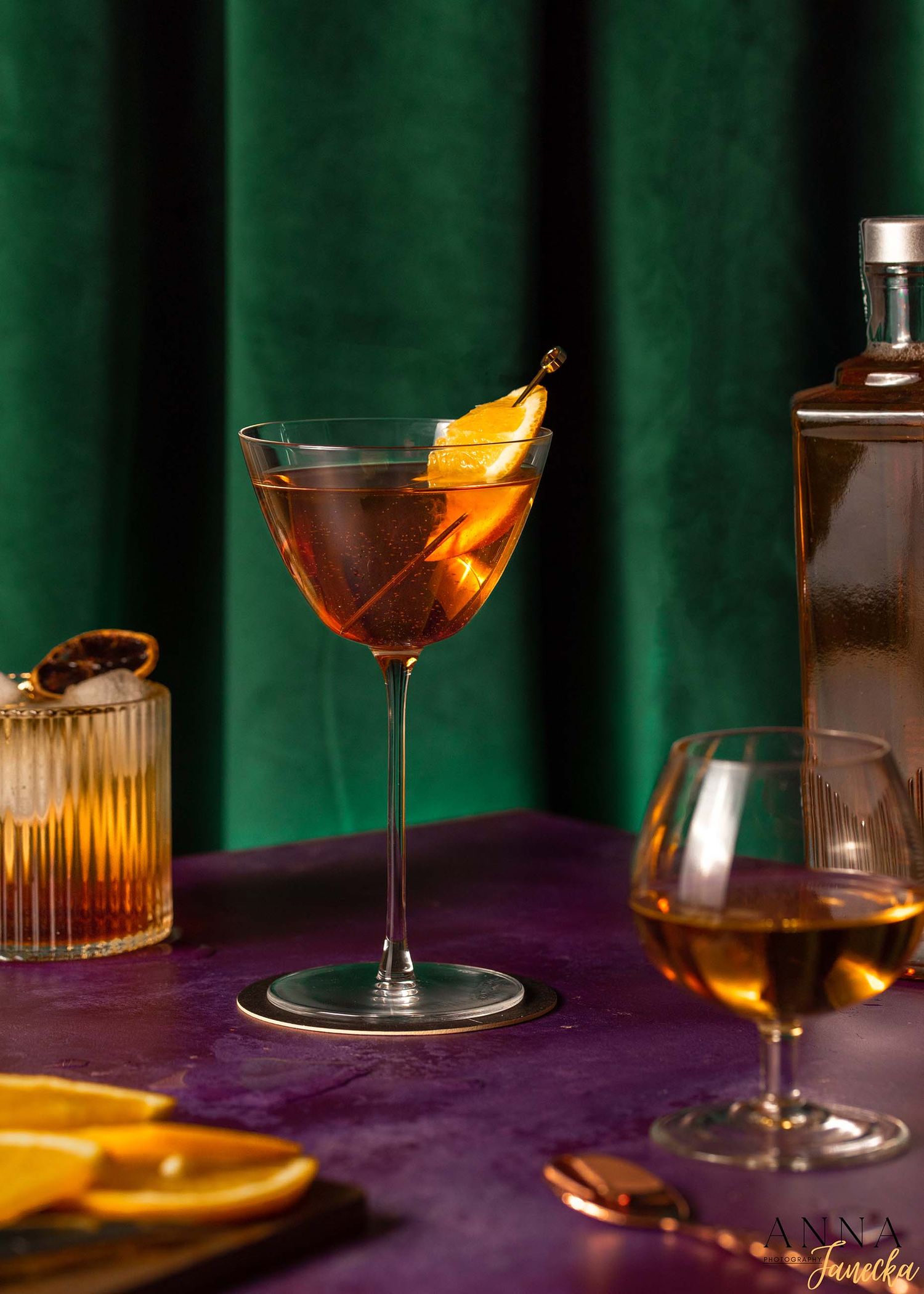 Elegant cocktails with orange garnish served in martini glasses against a green backdrop.