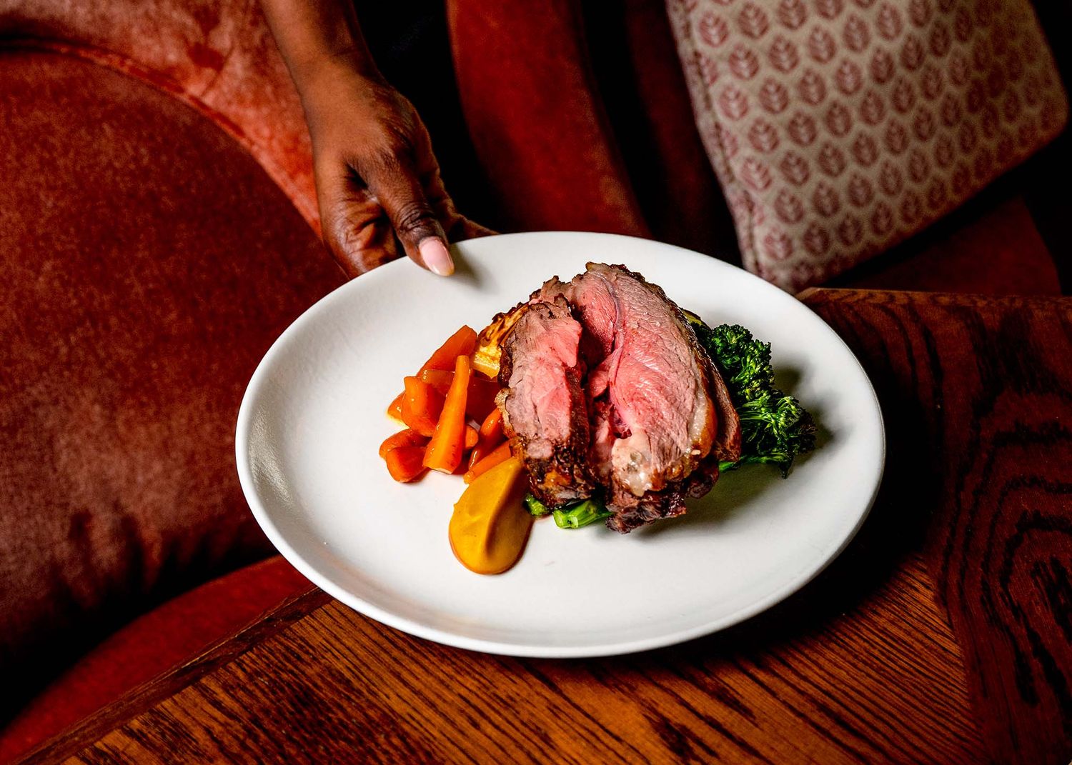 Perfectly cooked medium-rare prime rib served with roasted carrots and greens on a white plate.