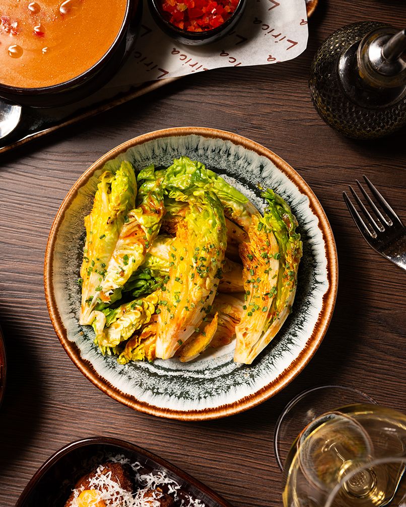 Grilled cabbage wedges garnished with fresh herbs and seasonings served on decorative plates with sauce on a wooden table.