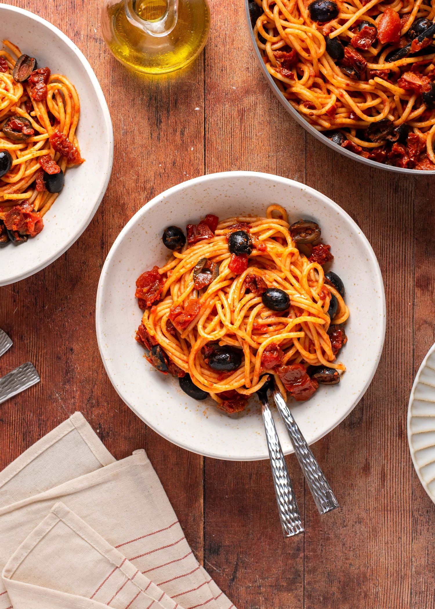 Spaghetti puttanesca with black olives, cherry tomatoes, and capers served in white bowls on a rustic wooden table.
